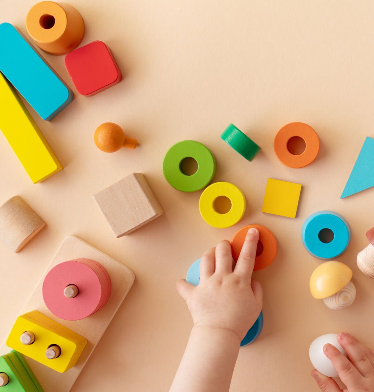 Toddler activity for motor and sensory development concept. Baby hands with colorful wooden toys on table from above.